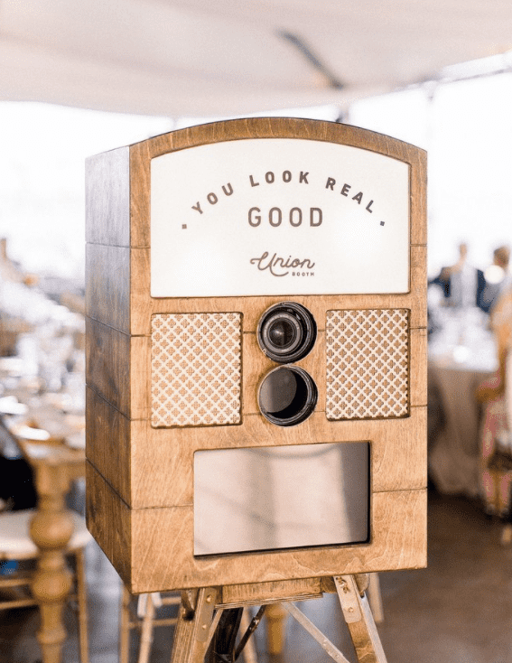 Photo booth camera encased in rustic wood finishes on top of a tripod stand