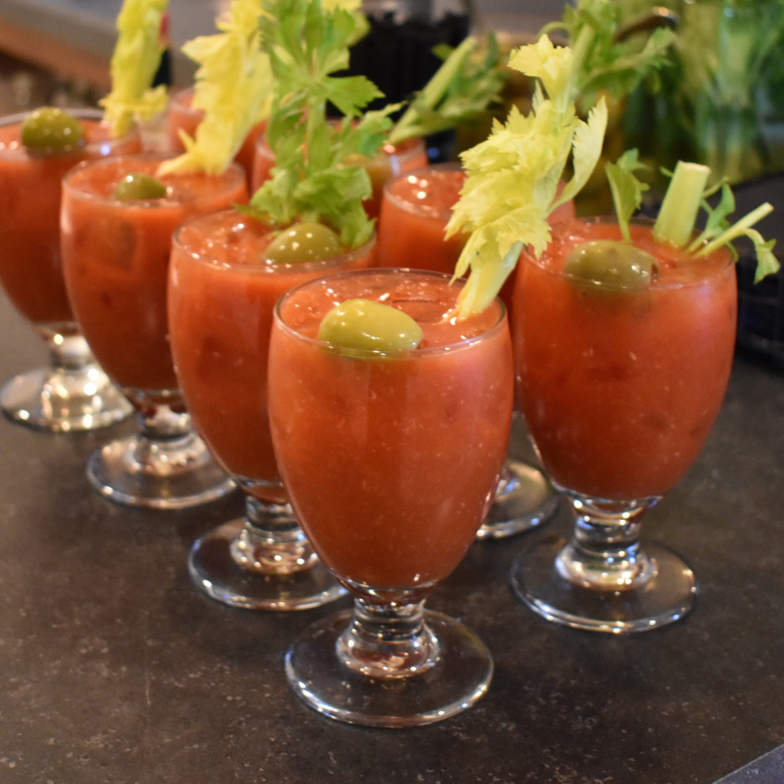 Group of bloody mary drinks topped with celery stalks in wine glasses