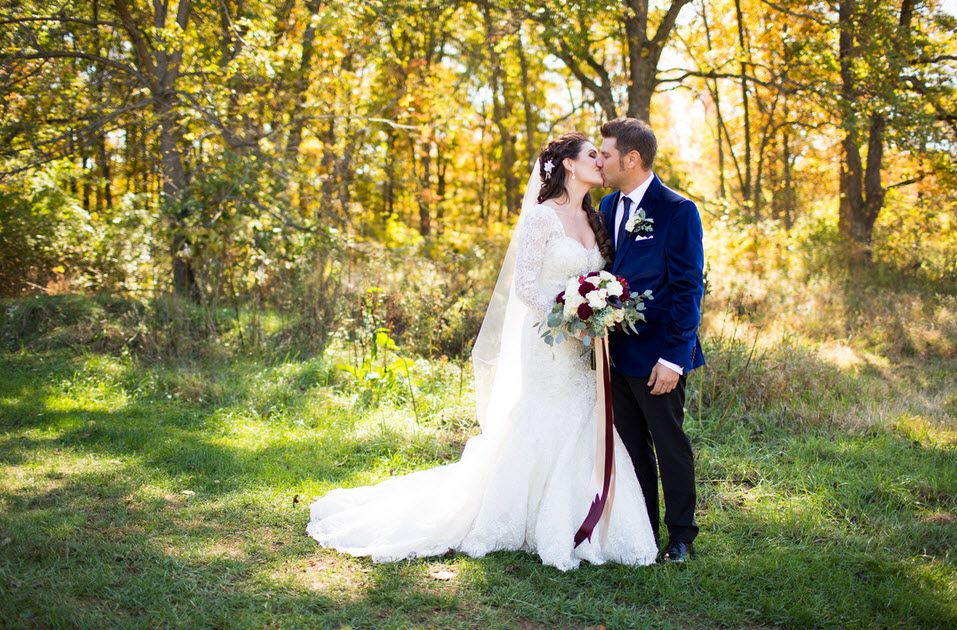 A wedding couple kissing surrounded by trees and green grass